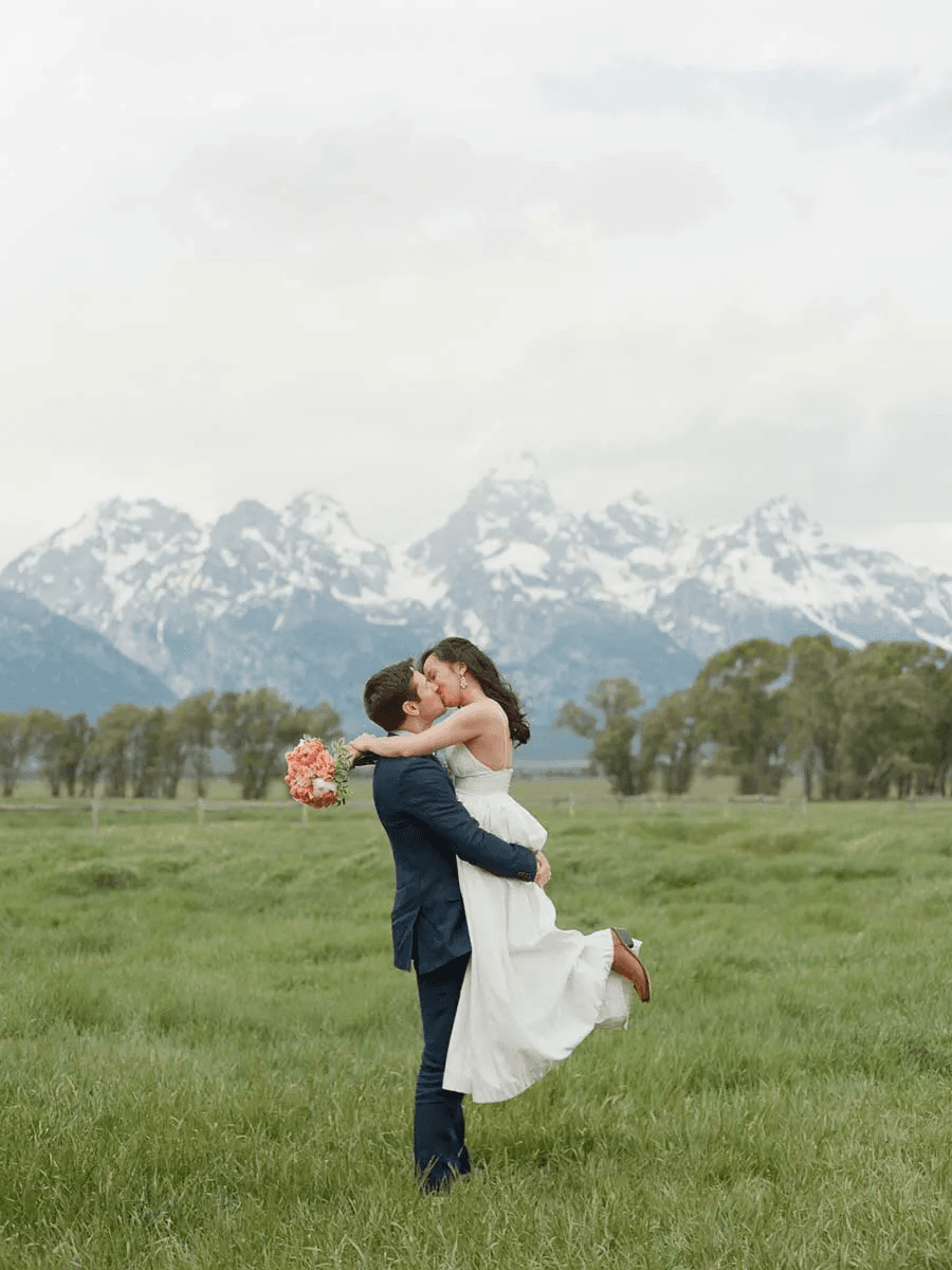A bride and groom embracing in a field during their wedding with the mountains in the background at a Noble House property