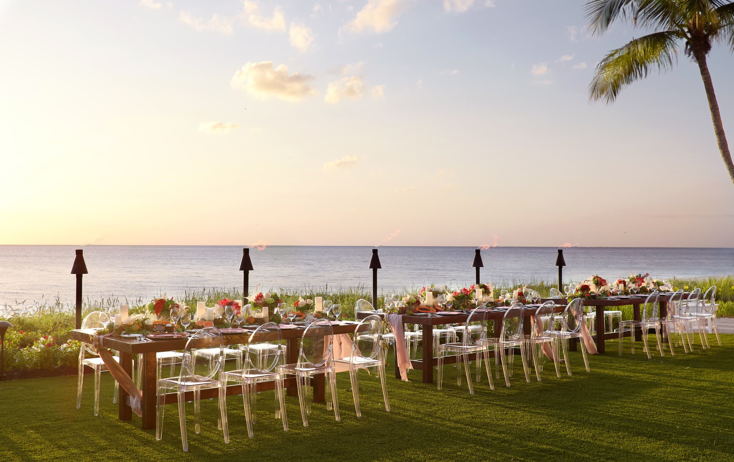 Tables set for a wedding with floral arrangements by the water at a Noble House Hotels & Resorts property