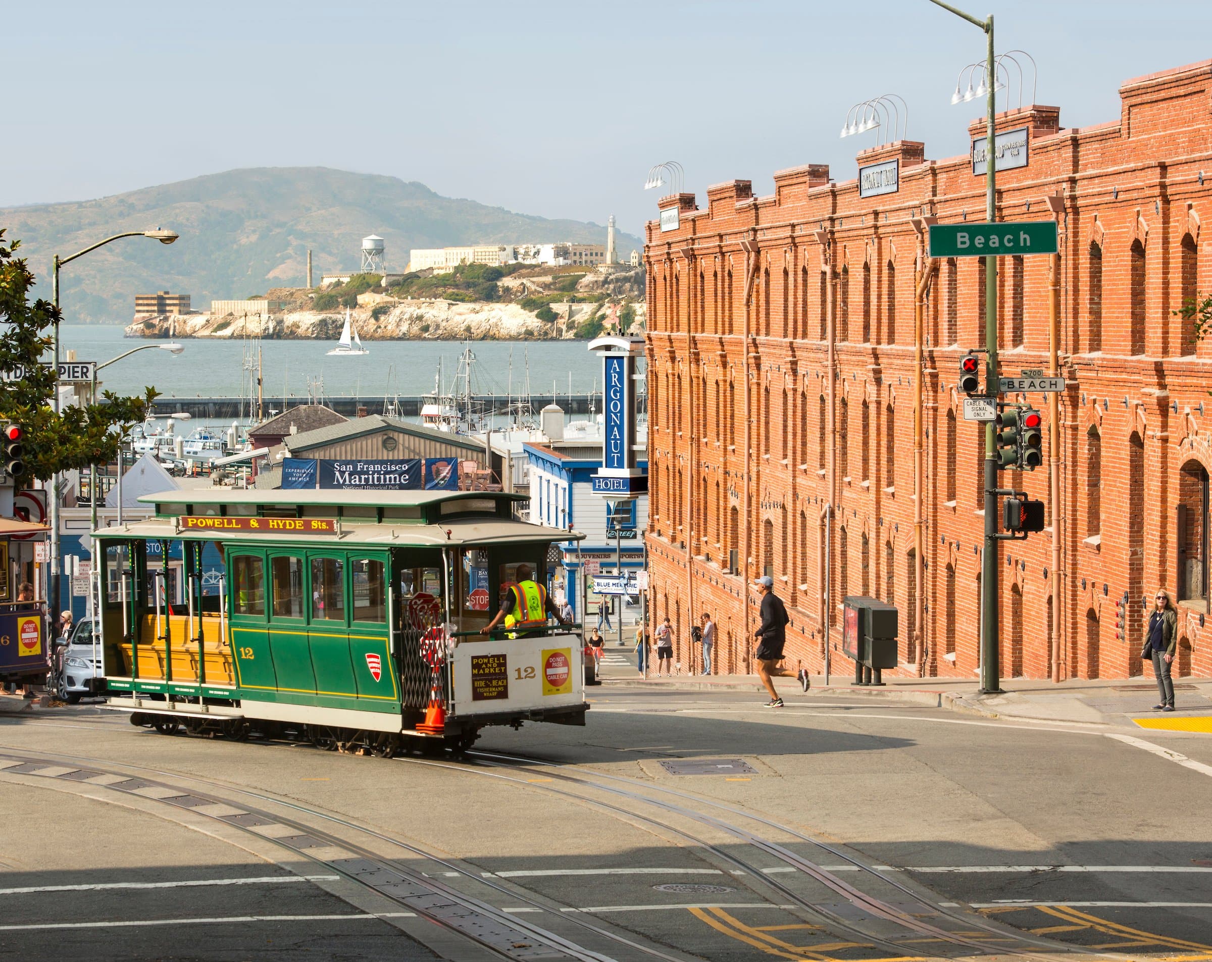 A cable car in the middle of the street out front of the San Fransisco Maritime National Historic park