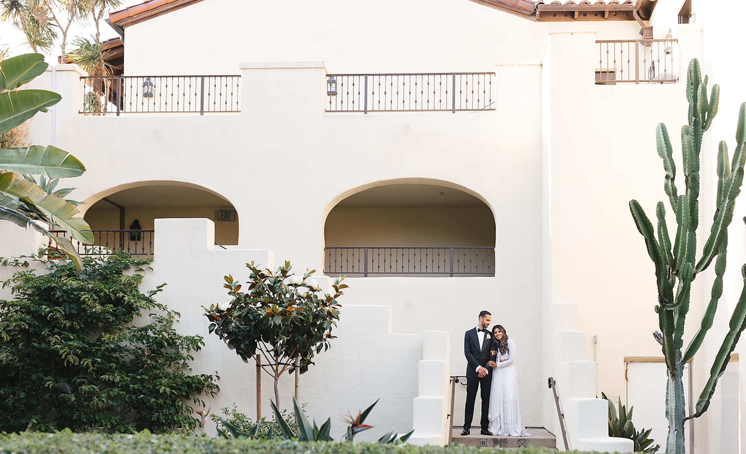 Wahid & Mehtaab standing in front of a large white Noble House Hotels & Resorts property getting their wedding photos done