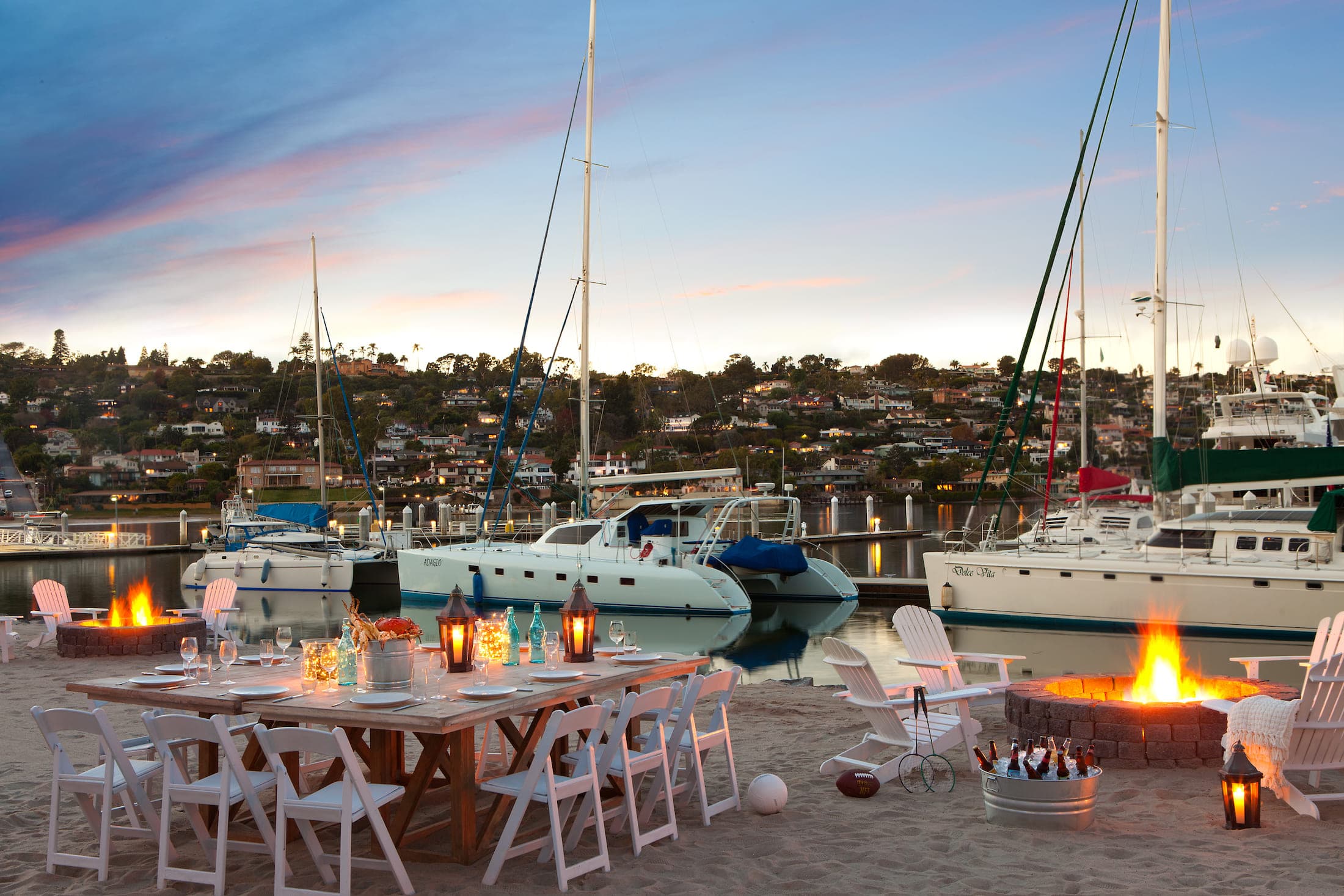 The marina area of Kona Kai San Diego with a large table setup for an event and a fire pit with a chairs around it and a bucket of beer on ice